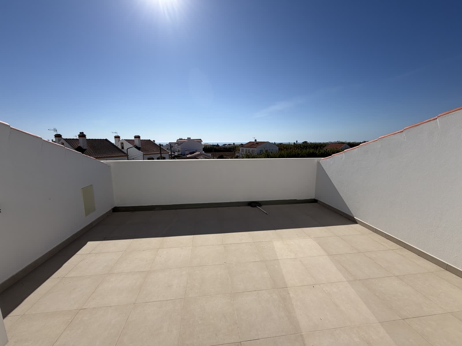 Het dakterras met witte muren; over de daken heen een strook zee aan de horizon.